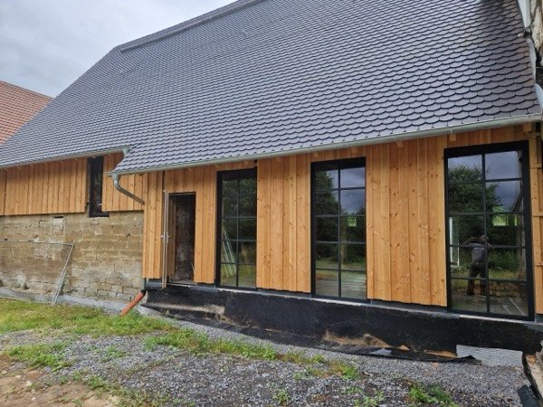 Gebäude mit Fassade aus senkrechten Holzbrettern und großen, schwarz gerahmten Fenstern.