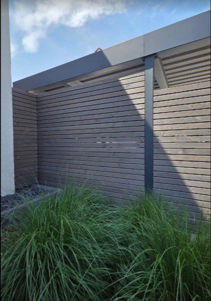 Über Eck laufende Sichtschutzwand aus waagerechten Holzlamellen mit dunklen Metallpfosten, davor Ziergräser.